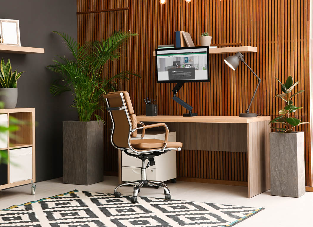 Comfortable workplace with computer near wooden wall in stylish room interior. Home office design